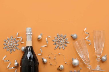 Gözlüklü şampanya şişesi ve turuncu arka planda Noel süsü.