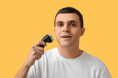 Sarı arka planda elektrikli traş makinesi olan yakışıklı bir genç.