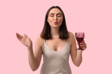 Kırmızı şarap kadehiyle güzel genç bir kadın pembe arka planda öpüşüyor.