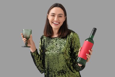 Gri arka planda cam ve şarap şişesi olan güzel genç bir kadın.