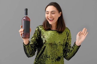 Gri arka planda şarap şişesi olan güzel genç bir kadın.