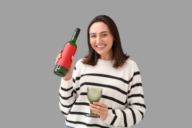 Gri arka planda cam ve şarap şişesi olan güzel genç bir kadın.