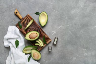 Kesik taze avokadoları ve gri arka planda yaprakları olan ahşap tahta bir tahta.