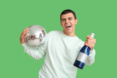 Mutlu genç adam disko topu ve bir şişe şampanyayla Noel 'i yeşil arka planda kutluyor.