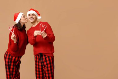 Mutlu genç çift Noel pijamaları ve bej arka planda şeker kamışları ile