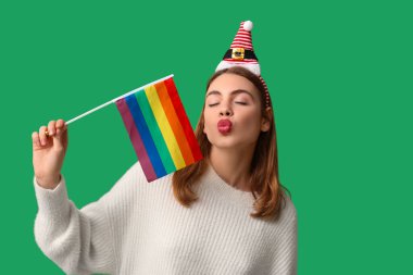LGBT bayrağıyla yeşil arka planda öpüşen Noel Baba şapkalı genç kadın.