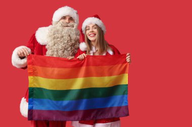 Kırmızı arka planda LGBT bayrağı olan Noel Baba kılığındaki genç çift.