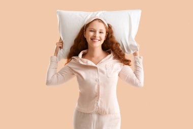 Bej arka planda beyaz yumuşak yastıklı mutlu genç kadın.