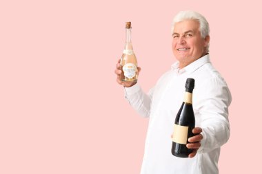 Elinde şampanya şişeleriyle kıdemli bir adam pembe arka planda Noel 'i kutluyor.