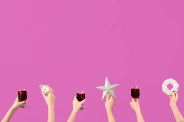 Sıcak şarap kadehleriyle kadın elleri ve pembe arka planda Noel dekoru.