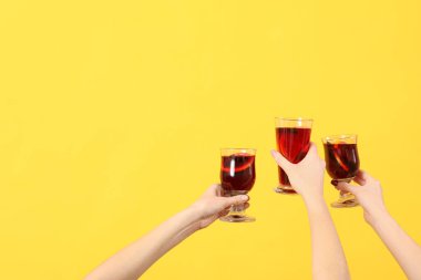Sarı arka planda sıcak şarap kadehleriyle kadın elleri.