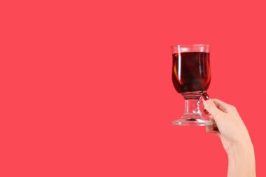 Kırmızı arka planda sıcak şarap kadehiyle kadın eli.