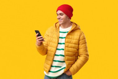 Şık kabarık ceketli ve sarı arka planda cep telefonu olan genç bir adam.