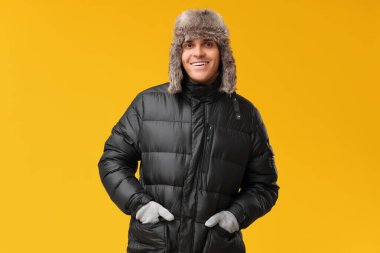 Sarı arka planda siyah renkli kabarık ceketli ve şapkalı genç adam.