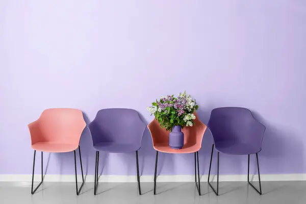 Stylish armchairs with beautiful lilac flowers near lilac wall