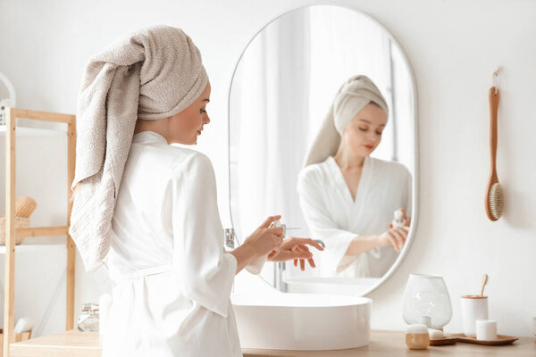 Young woman applying cream after shower near mirror in bathroom