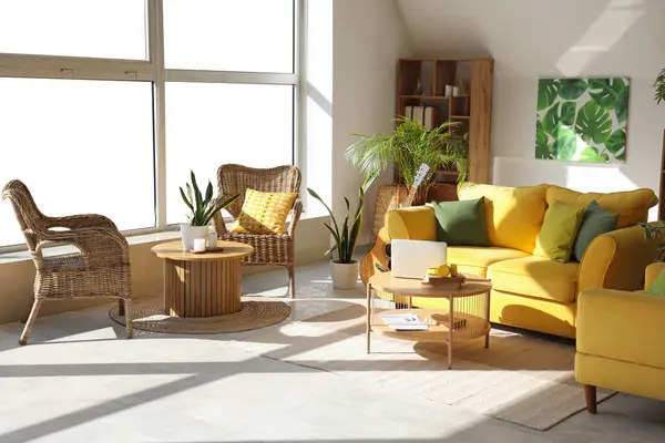 Interior of stylish living room with yellow sofa, laptop on table and houseplants
