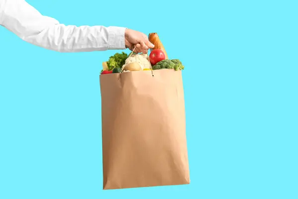 Woman holding paper bag with vegetables on blue background. Food delivery concept