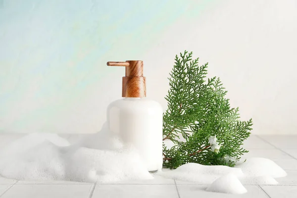 Bottle of skincare product with foam and coniferous branches on white tile table