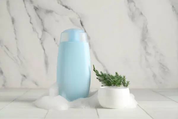 Skincare products with foam and coniferous branch on white tile table