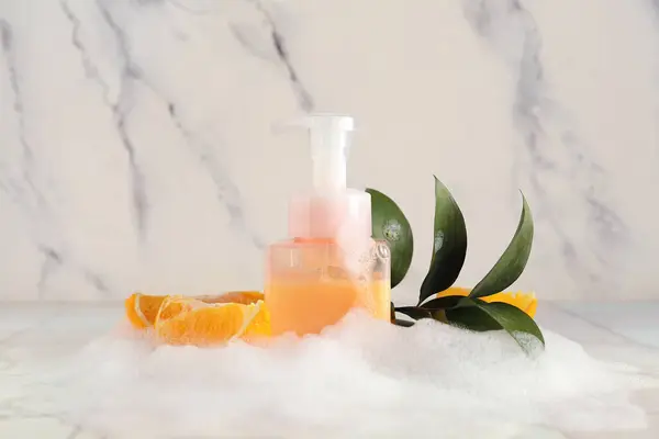Bottle of skincare product with foam, orange and plant branch on table