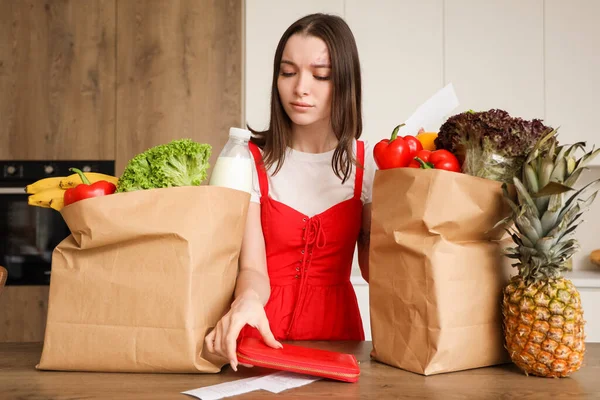 Young woman with bags of food and store receipt in kitchen. Price rise concept