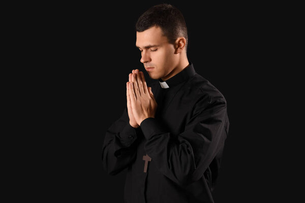 Young priest praying on dark background