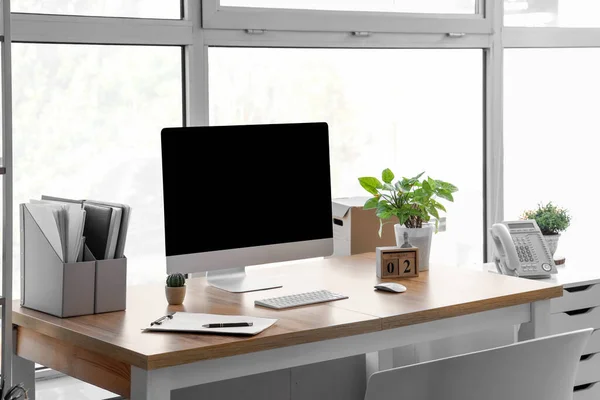 Blank computer monitor with folders and plants near window in office