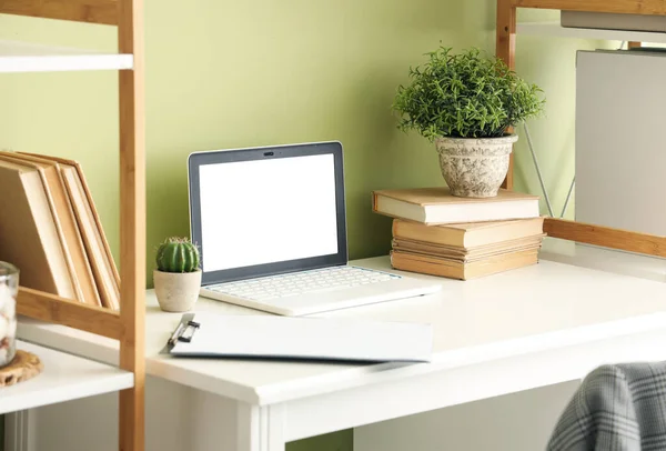 Blank laptop with books and plants on table in office