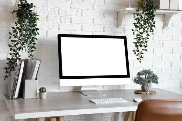 Blank computer monitor with plants on table in light office