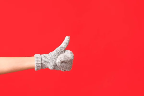 Hand in warm glove showing thumb-up on red background