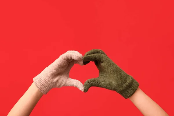 Hands in warm gloves making heart on red background