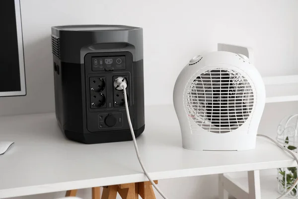 Electric fan heater plugged in portable power station on white table, closeup