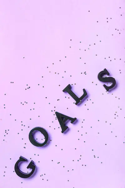 Word GOALS with confetti on lilac background