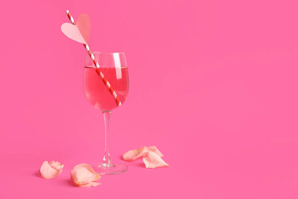 Glass of tasty cocktail with straw and rose petals on pink background. Valentine's Day celebration