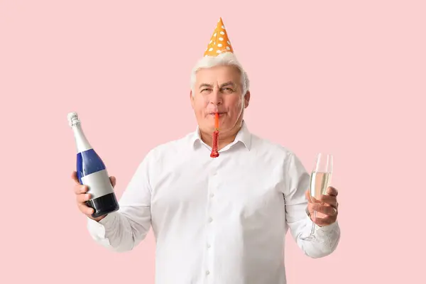 Senior man in party hat with bottle and glass of champagne celebrating Christmas on pink background
