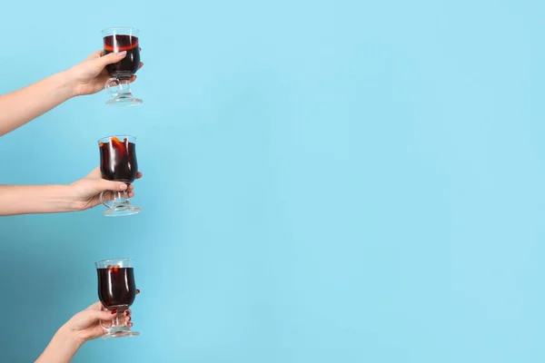 Female hands with glasses of warm mulled wine on blue background