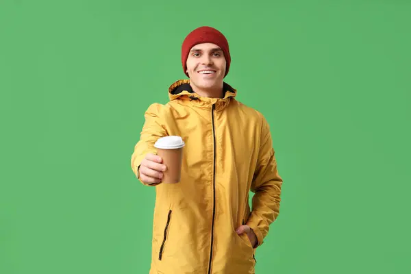 身穿黄色时髦夹克 头戴黄帽 头戴绿底纸杯咖啡的年轻人 — 图库照片