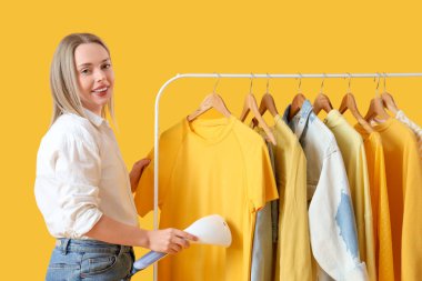 Güzel, genç bir kadın, sarı arka planda modern buharlı giysiler giyiyor.