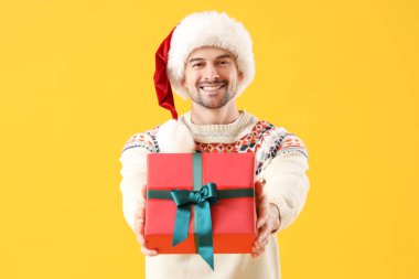 Sarı arka planda Noel Baba şapkalı yakışıklı bir adam.