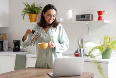 Modern mutfakta gayzer kahve makinesi ve bir fincan espresso kullanan güzel genç bir kadın.