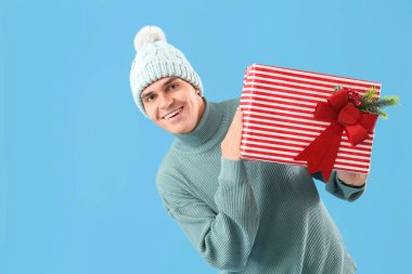 Mavi arka planda Noel hediyesi olan mutlu genç adam.