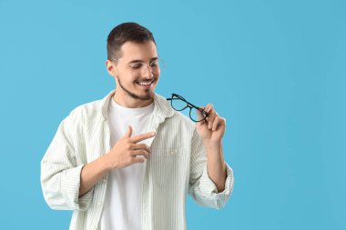 Genç adam mavi arka plandaki gözlüklere bakıyor.