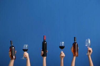 Mavi arka planda şarap şişeleri ve bardaklarla kadın elleri