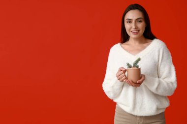 Kırmızı arka planda sıcak şarap kadehiyle mutlu genç bir kadın.