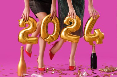 2024 figürlü genç kadın bacakları, pembe arka planda şampanya ve parti dekoru. Yeni yıl kutlaması