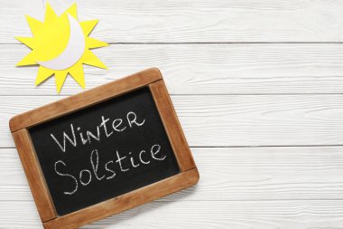 Yazılı tebeşir tahtası Kışlık SOLSTICE ve beyaz ahşap zemin üzerinde kağıt güneş