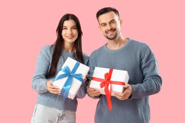 Pembe arka planda Noel hediyeleri olan genç bir çift.