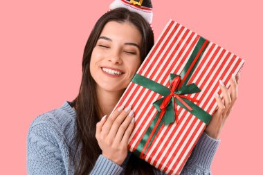 Noel Baba şapkalı genç kadın pembe arka planda Noel hediyesi, yakın plan.