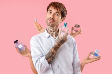 Dövmeli genç adam ve elleri pembe arka planda parfüm şişeleriyle dolu.